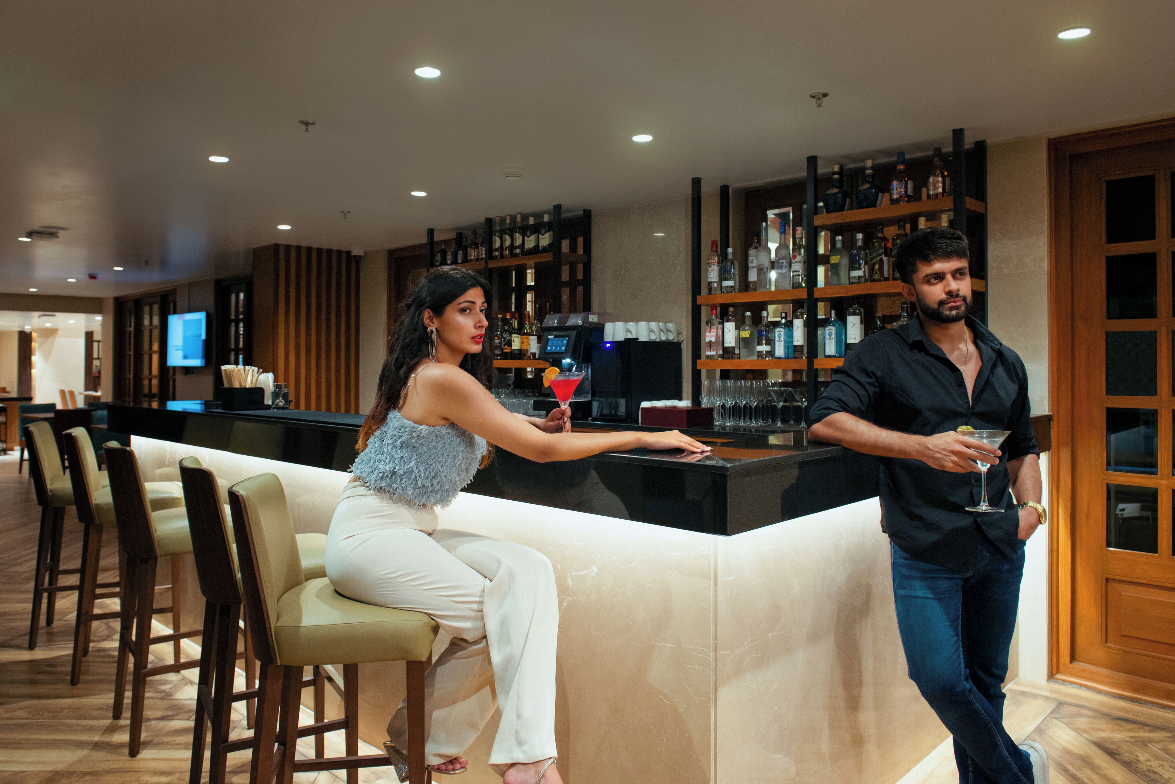 A bar area with a counter, bar stools, and a television screen in the background.