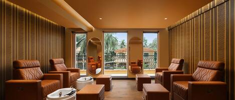 A spa room with multiple massage chairs, a white bathtub, and large windows offering a view of palm trees and a balcony.