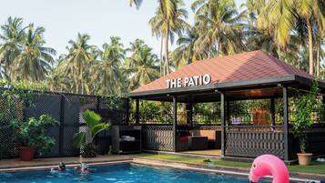 A swimming pool with a pink flamingo float, surrounded by palm trees and a covered area labeled "THE PATIO".