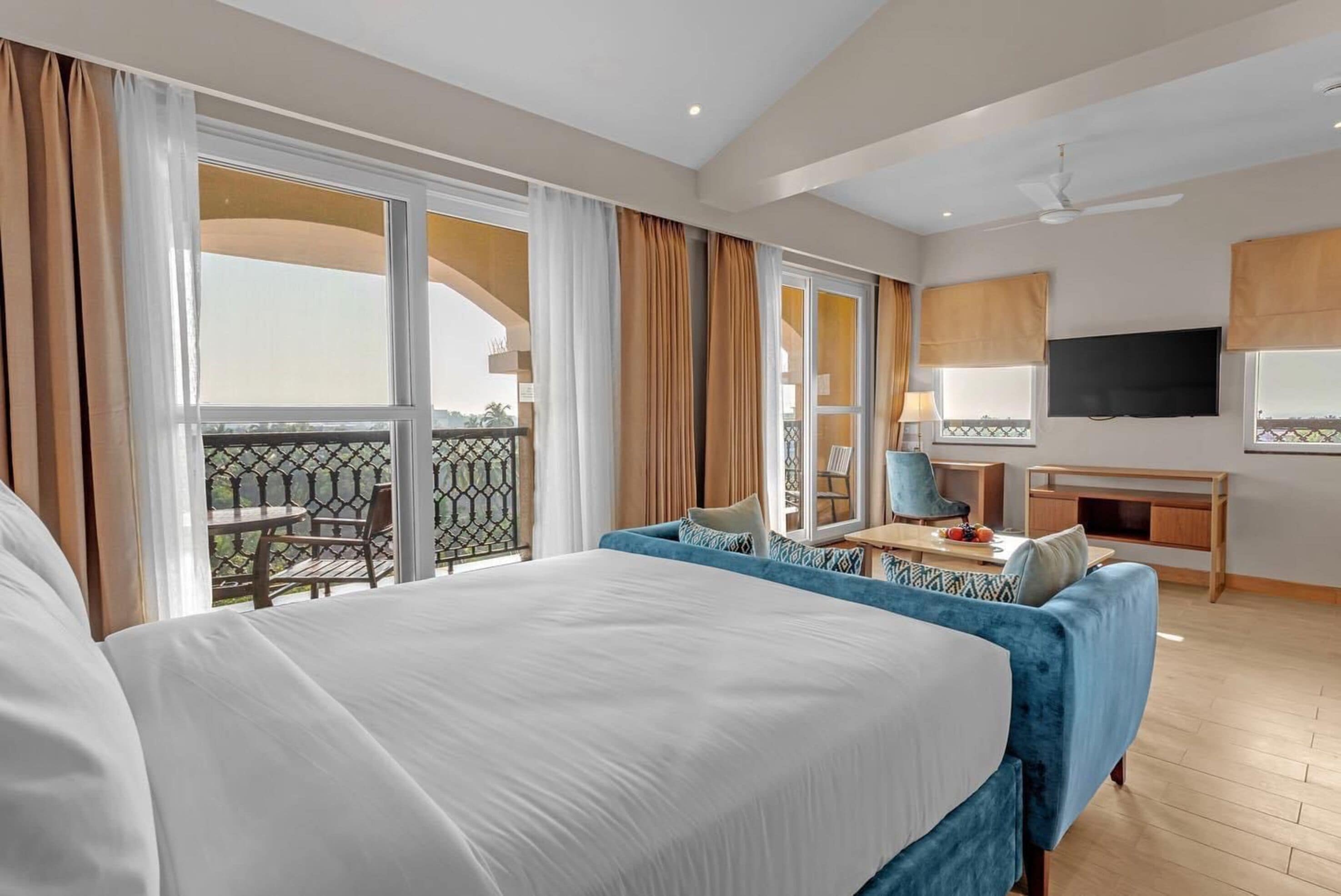Hotelkamer met een groot bed, een bureau met stoel, een televisie en een balkon met tafel en stoelen.