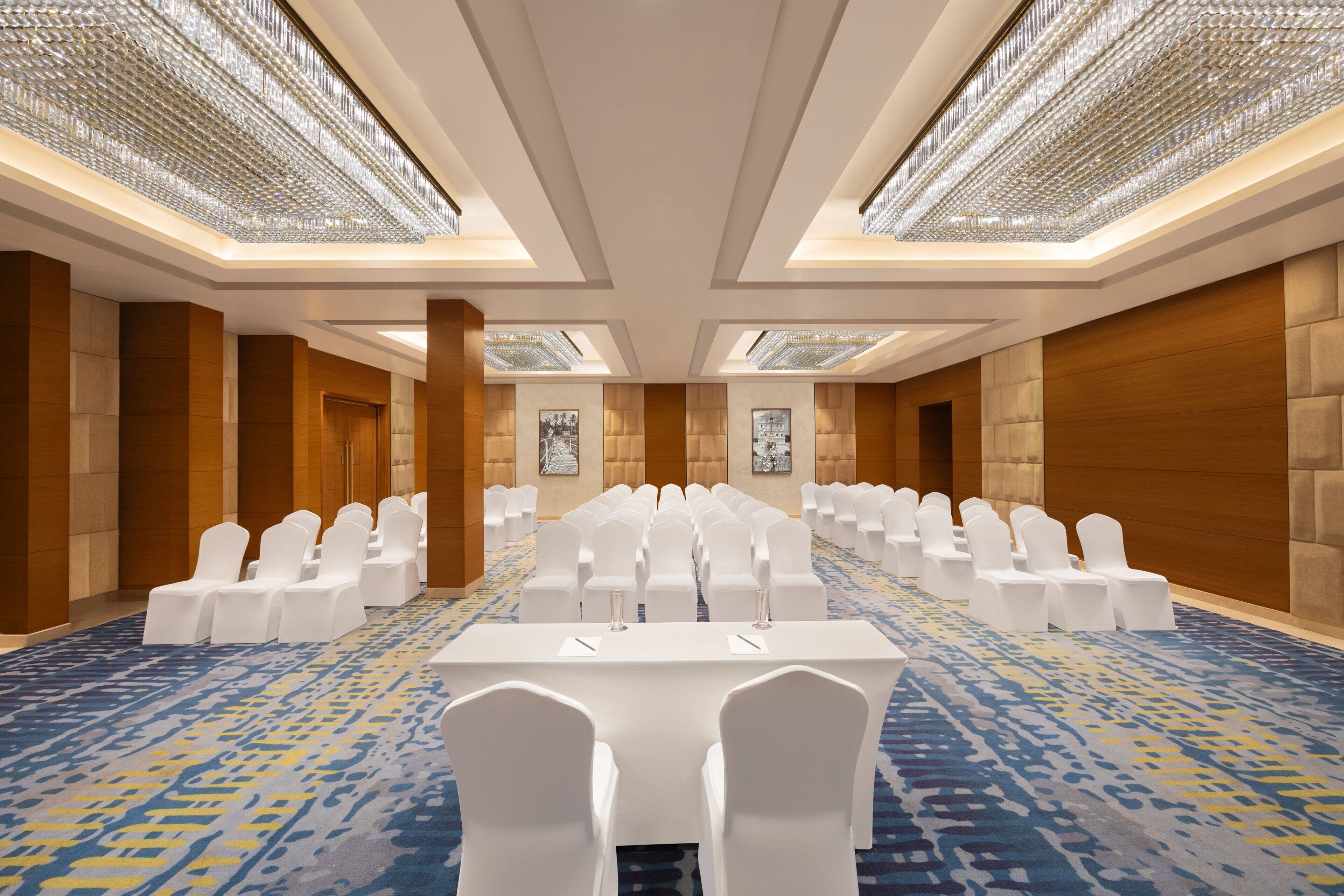 A conference room with a long table, white chairs, and a patterned carpet.