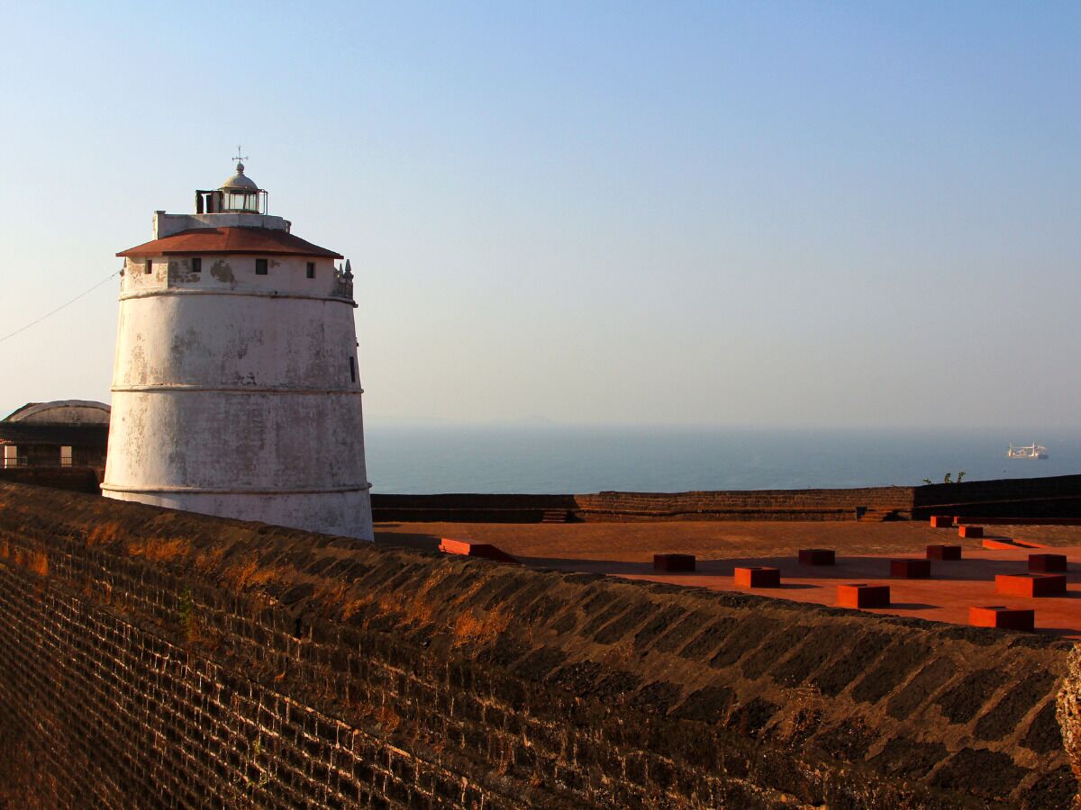 A lighthouse with a circular base and a dome on top, situated on a coastal cliff with a clear view of the sea.