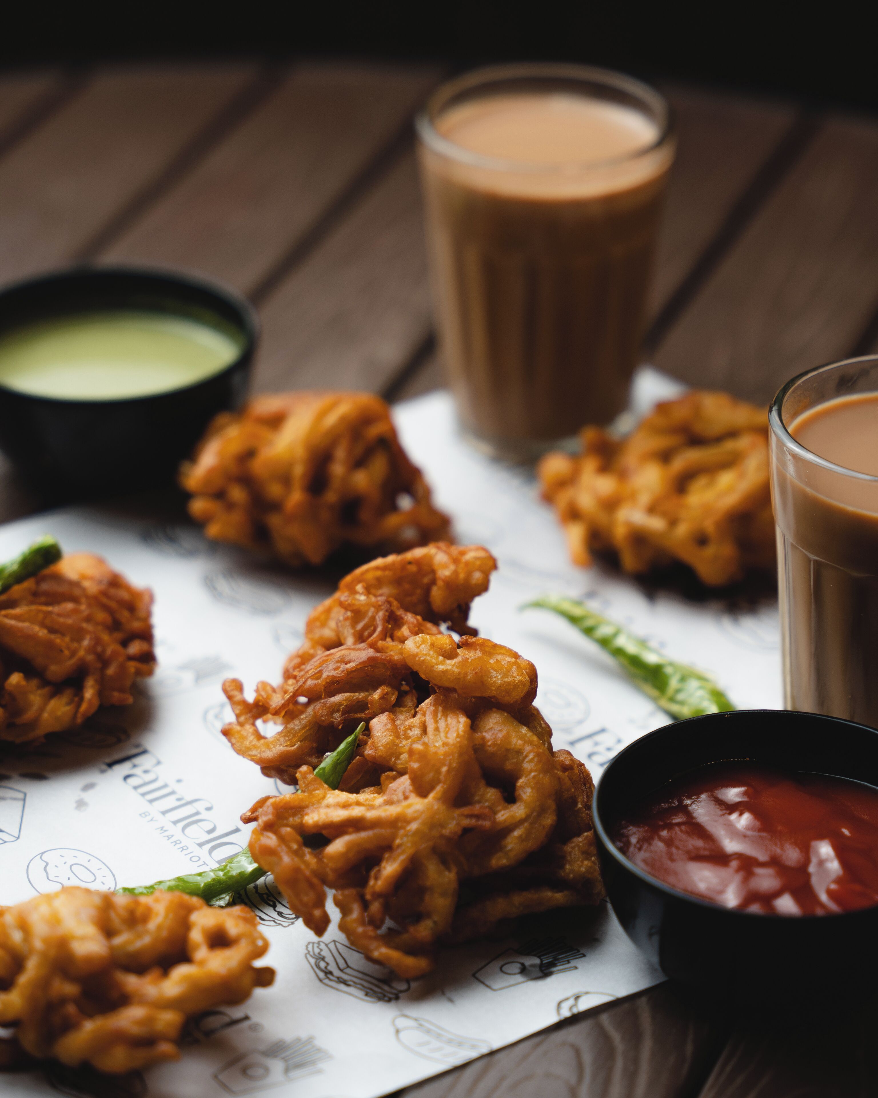A table with fried snacks, a glass of iced tea, and two bowls of sauces.