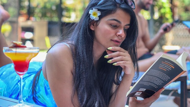 Una persona leyendo un libro en una mesa al aire libre con una bebida.