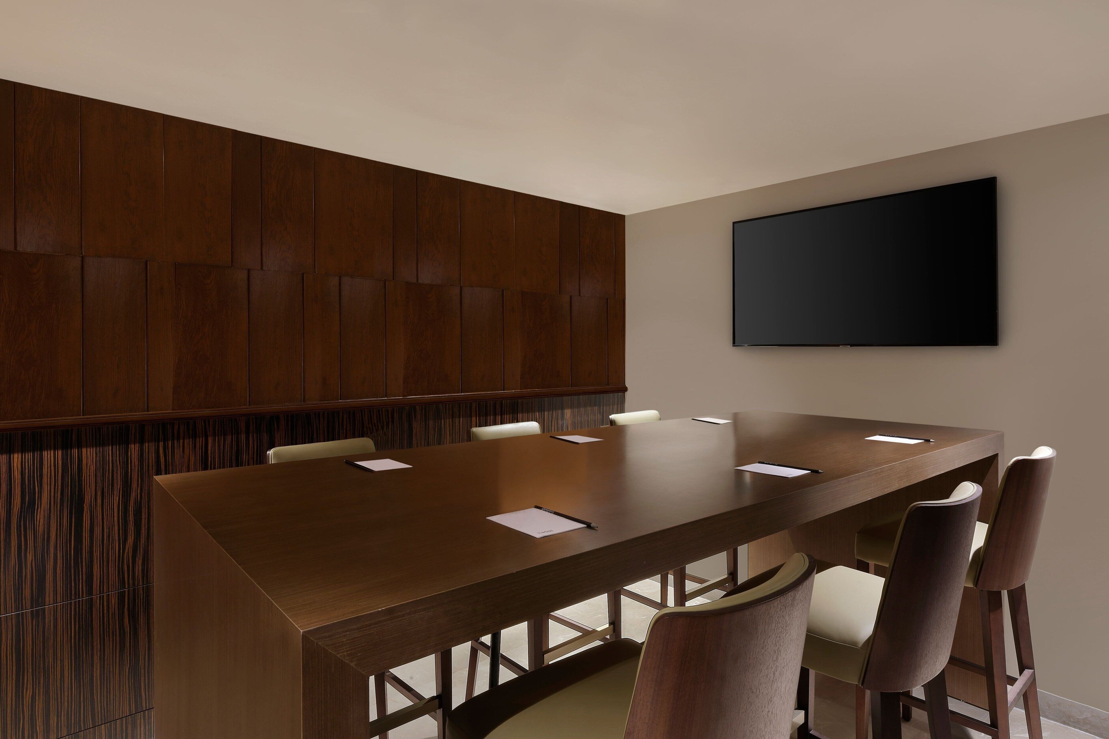 Uma sala de conferência com uma mesa comprida, seis cadeiras e uma televisão de tela plana fixada na parede.