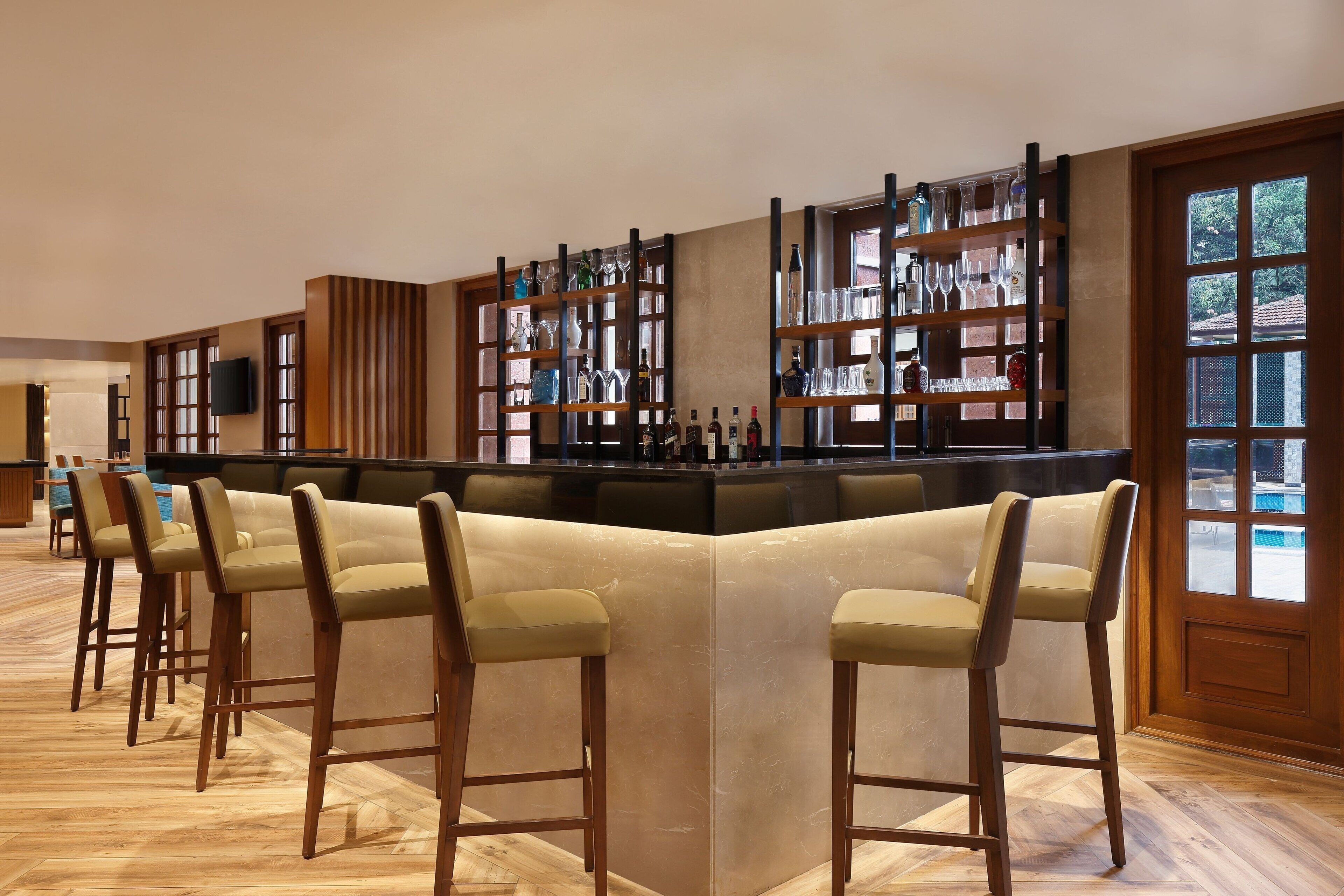 Zona de bar con taburetes de madera, estanterías llenas de botellas y vistas al exterior a través de amplias ventanas.
