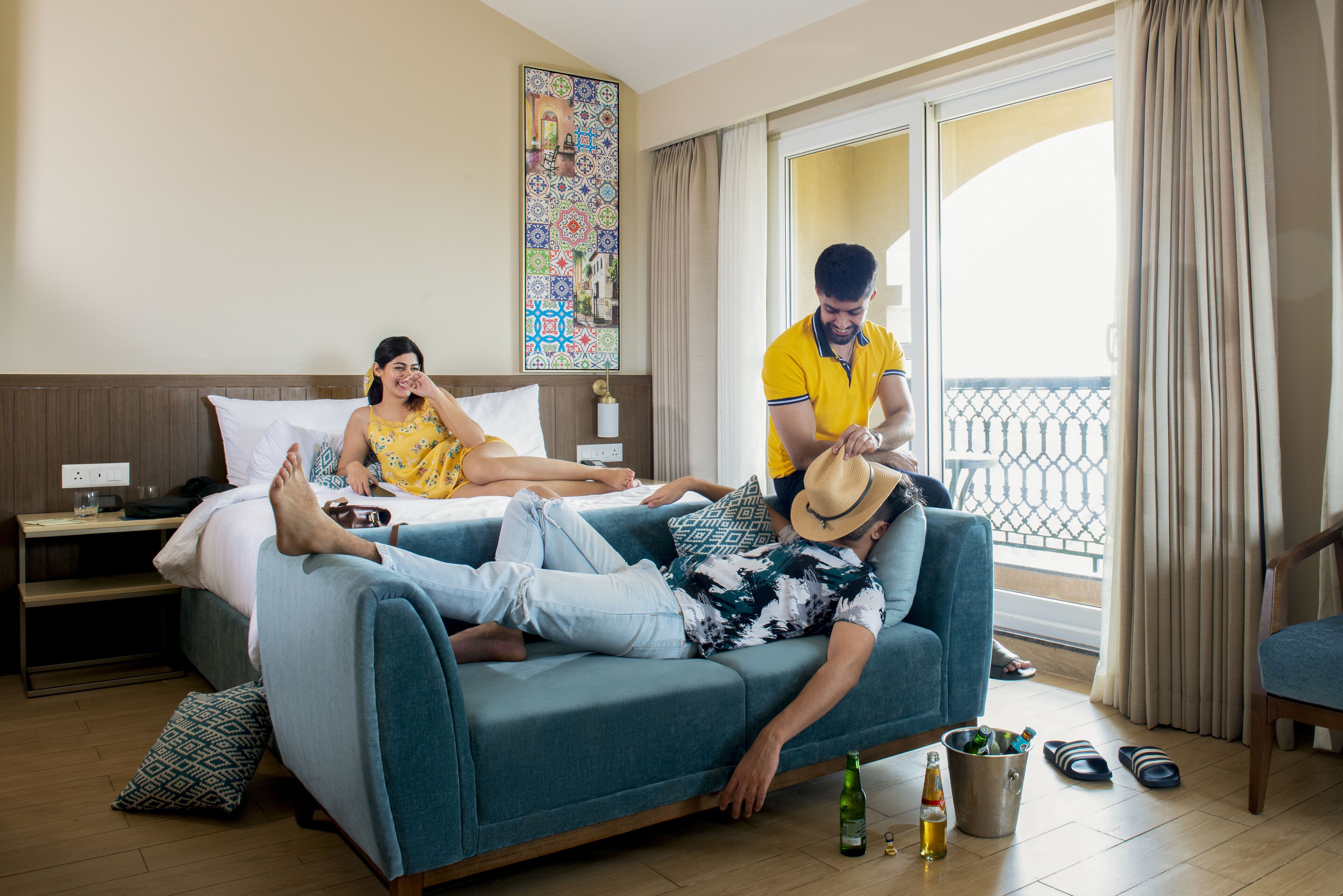 Una camera d'albergo con un letto, un divano, un comodino, una lampada, una finestra con tende e un balcone.