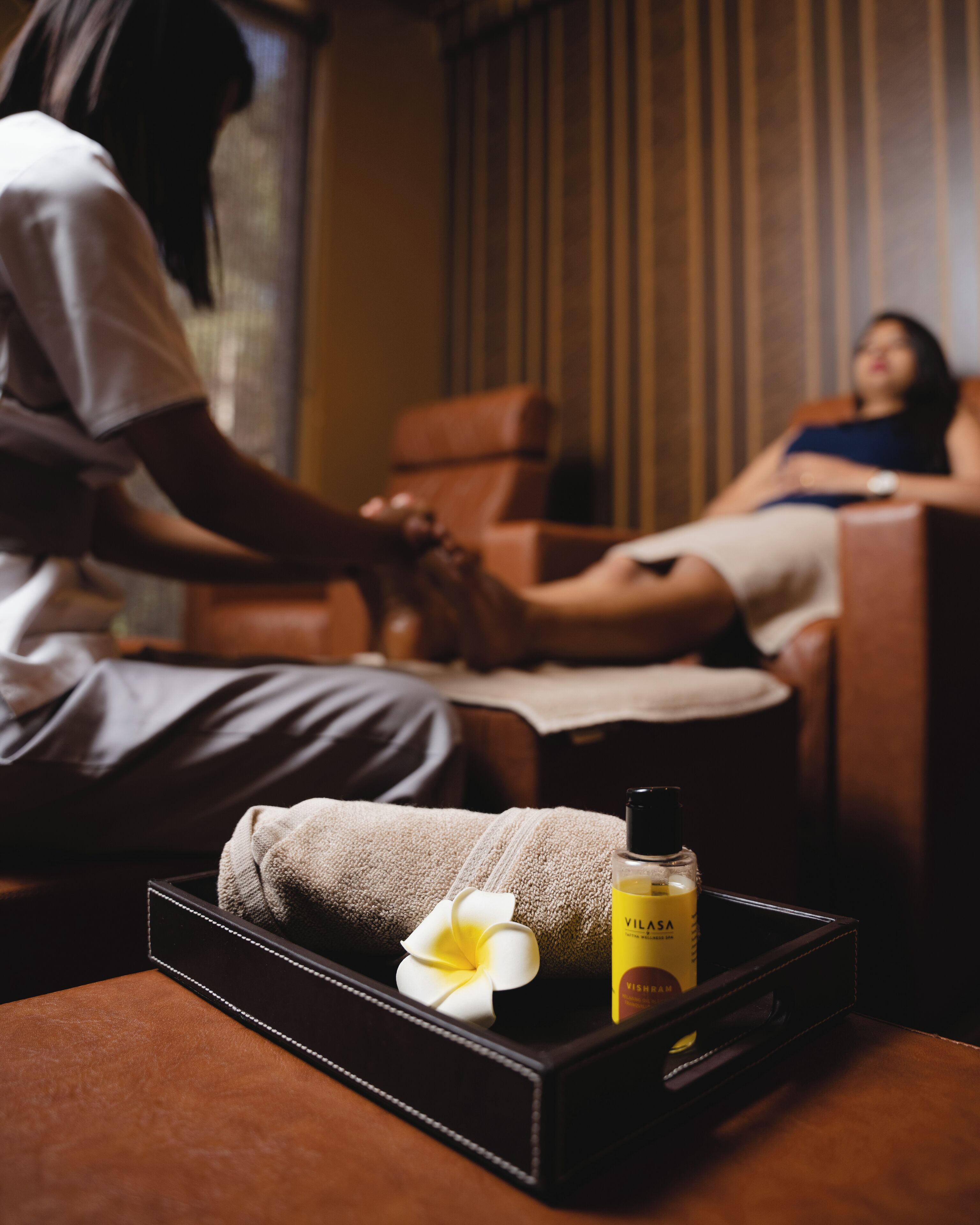 A massage therapy room with a massage table, a towel, a flower, and a bottle of oil.