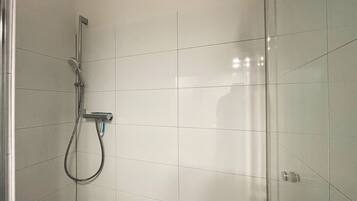 Un espacio con ducha, un cabezal de ducha de mano y un grifo instalado en la pared.