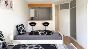 A modern bedroom with a bed, two black bar stools, a bedside table with a lamp, a framed picture on the wall, and a wardrobe with a mirror. - Schönes Apartment in Melle I home2share (Melle)