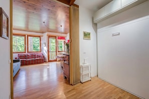 Een ruime kamer met houten vloeren, een rode bank, een houten plafond en grote ramen.