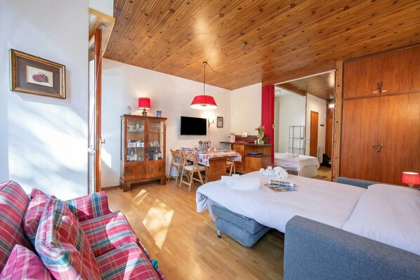 A cozy room with a bed, a sofa, a desk with a chair, a television, and a wardrobe.