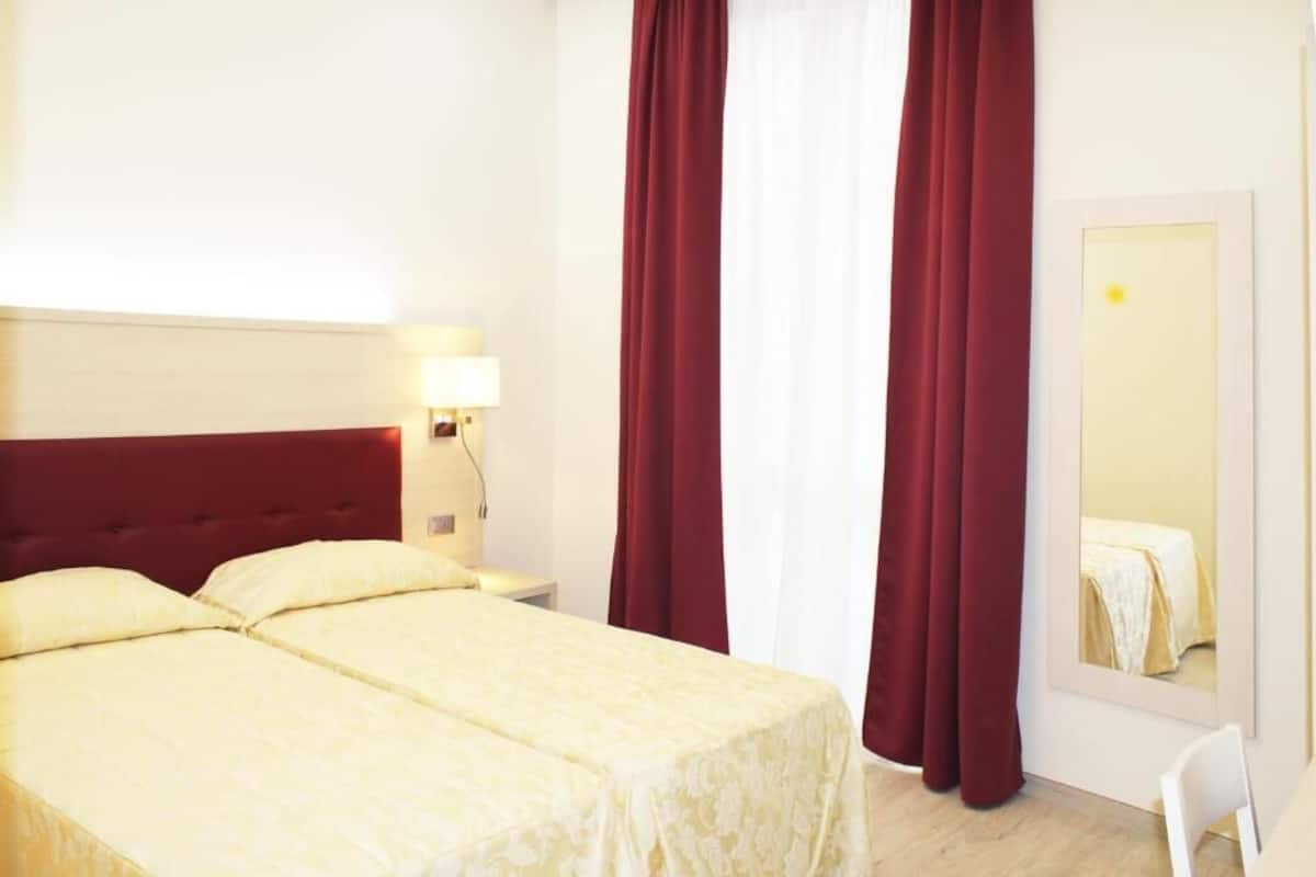 Una habitación de hotel con una cama, una mesita de noche, una lámpara y un espejo.