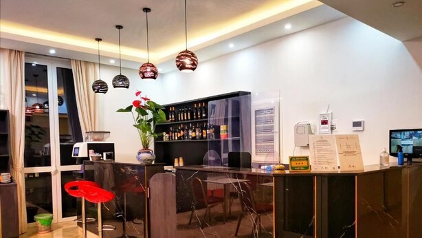 A modern reception area with a marble counter, red bar stools, a potted plant, a wine rack, and a digital information board. - CSI Group - Hotel metropoli (Milan)