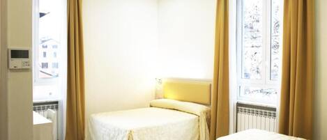Ein Hotelzimmer mit zwei Betten, einem kleinen Schreibtisch und einem Fenster mit Vorhängen.
