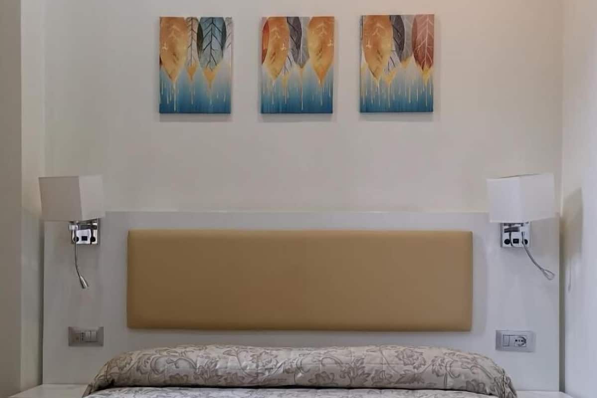 Una habitación de hotel con una cama, dos lámparas de pared y tres cuadros abstractos en la pared.