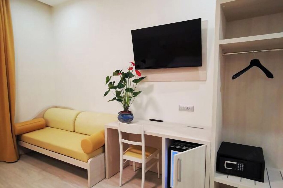 Un espace de vie compact comprenant un canapé, une petite table, une plante en pot, un téléviseur fixé au mur, une armoire et un porte-manteau suspendu.