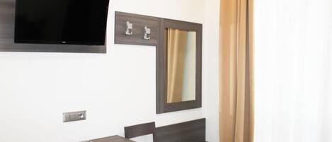 A modern bathroom with a mounted TV, a mirror, a vanity with a chair, and a curtain.