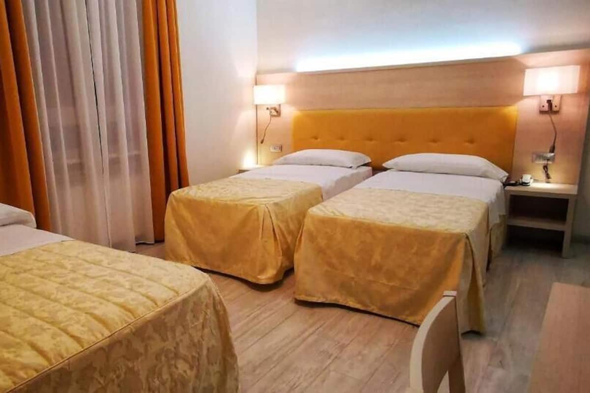 Habitación de hotel con dos camas, cabecera de madera, mesita de noche y una lámpara.