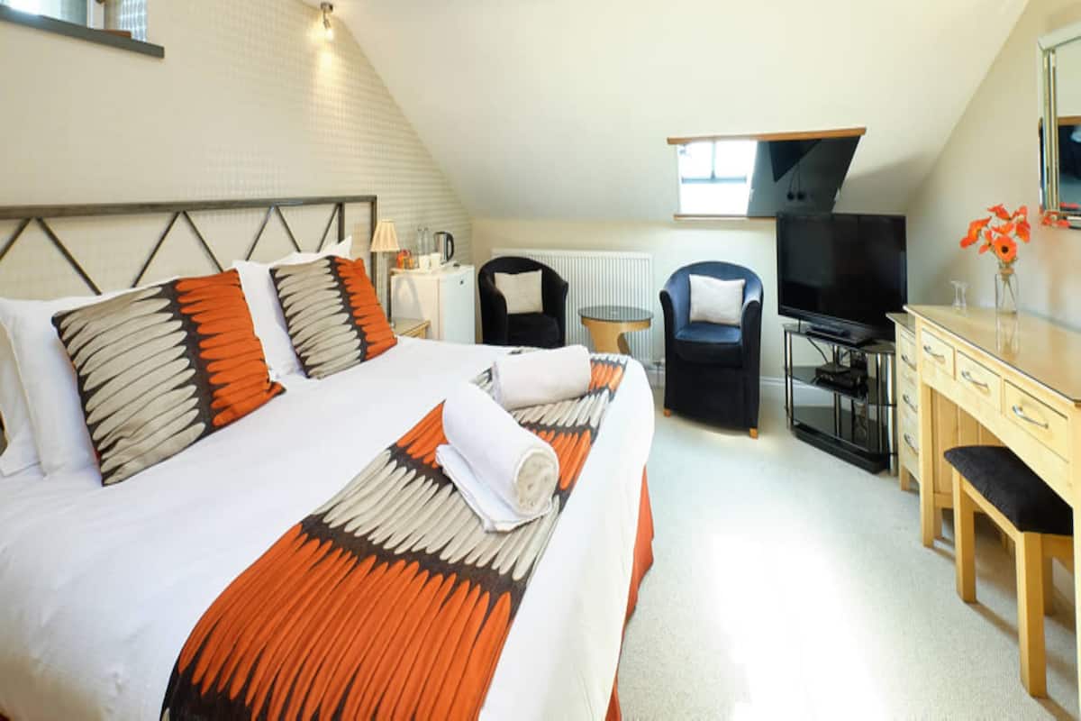 A hotel room with a large bed, a desk, a chair, a television, and a window.