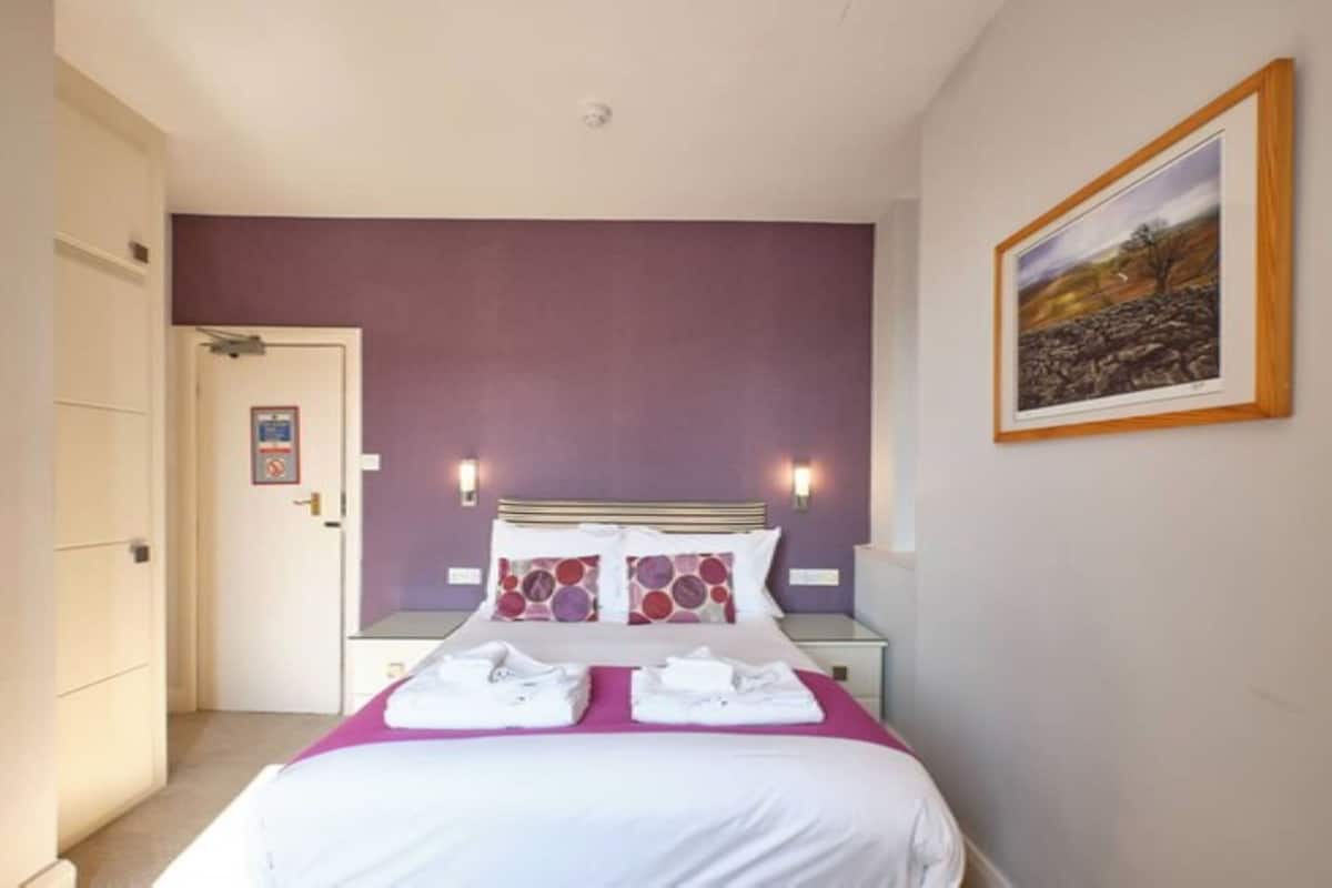 A hotel room with a bed, two bedside tables, a door, and a framed picture on the wall.