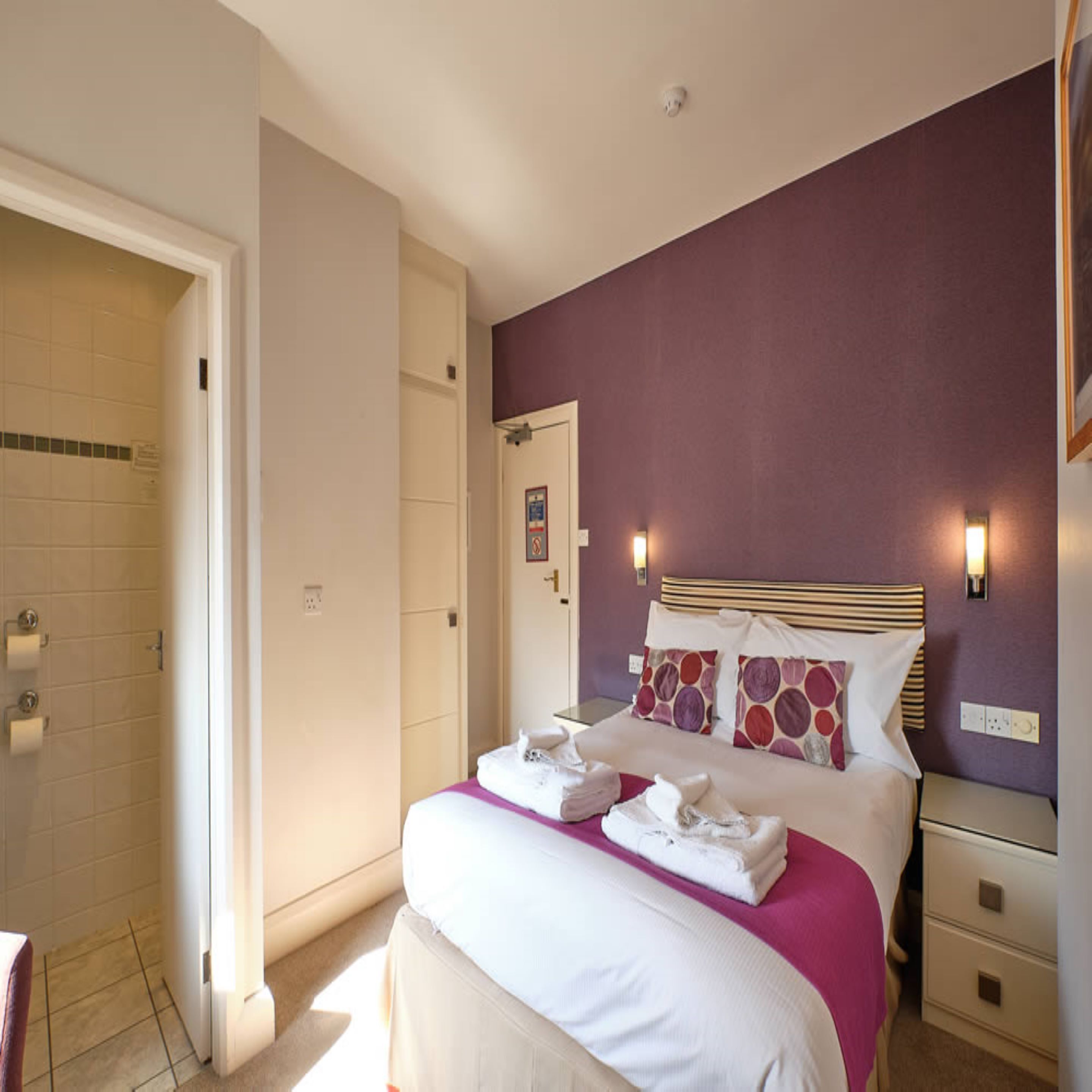 Une chambre d’hôtel avec un lit, une table de chevet, une salle de bain avec douche et une porte.