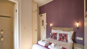 A hotel room with a bed, a nightstand, a bathroom with a shower, and a door.