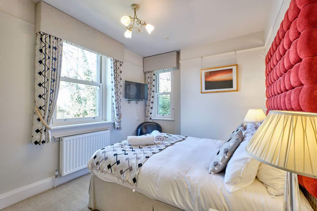 A bedroom with a bed, a chair, a TV, a lamp, and a window with curtains.