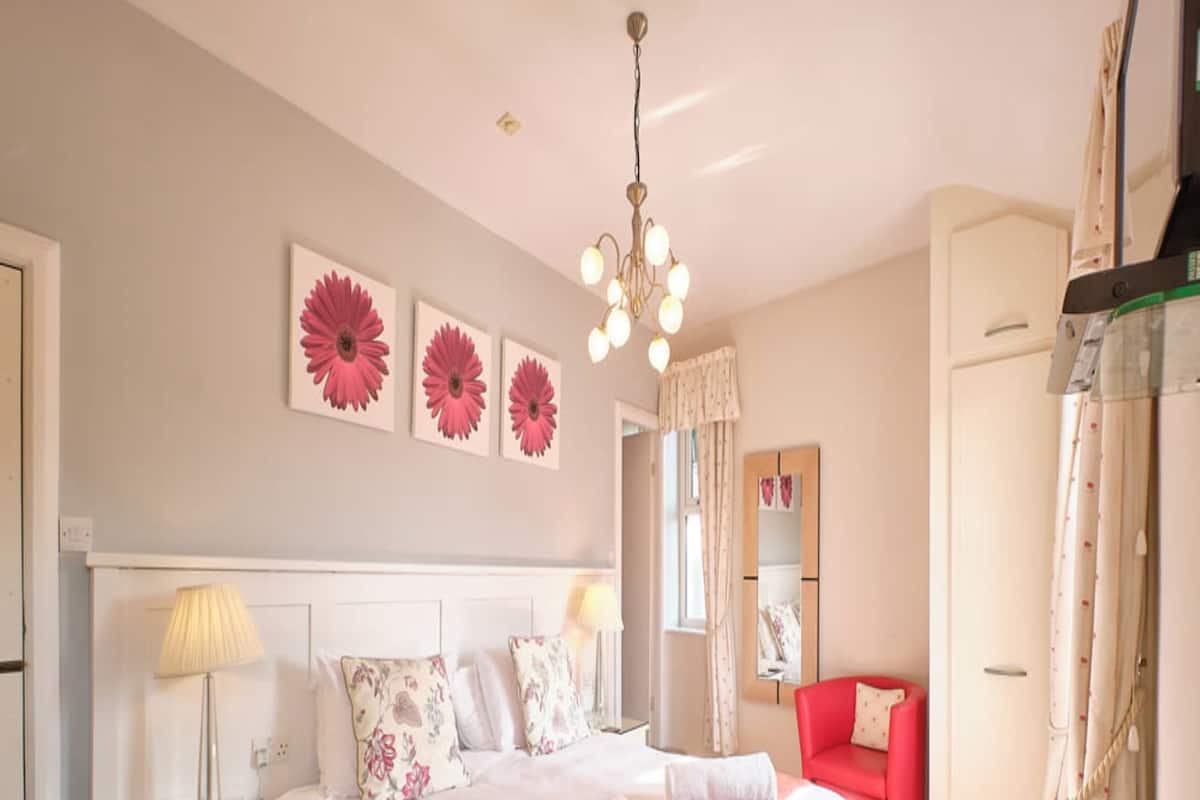 A bedroom with a bed, bedside tables, a red chair, a mirror, and a chandelier.
