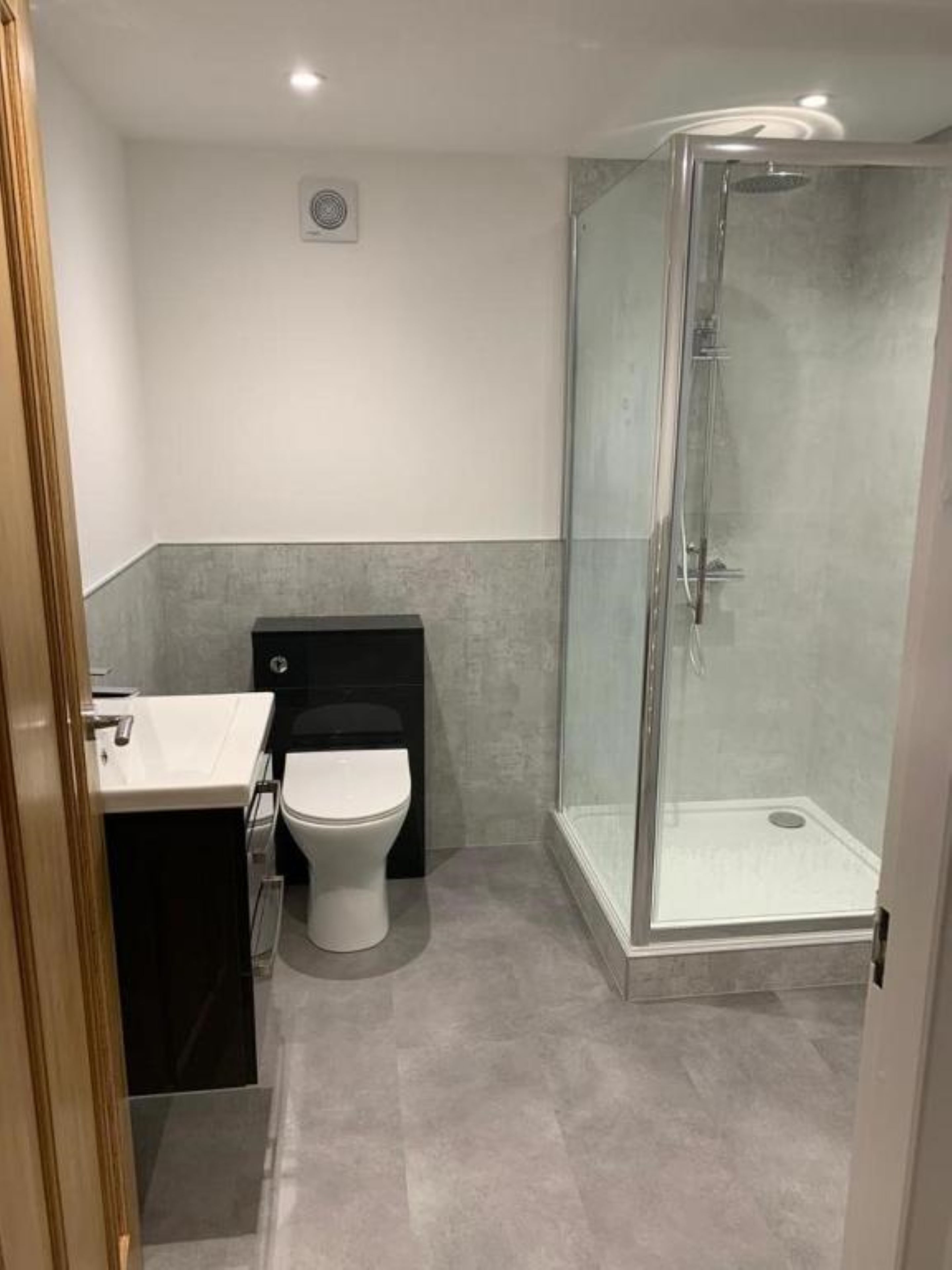 A modern bathroom with a glass-enclosed shower, a white toilet, and a dark-colored sink.