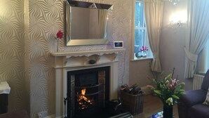 Una sala de estar con chimenea, un espejo encima y una ventana con cortinas.