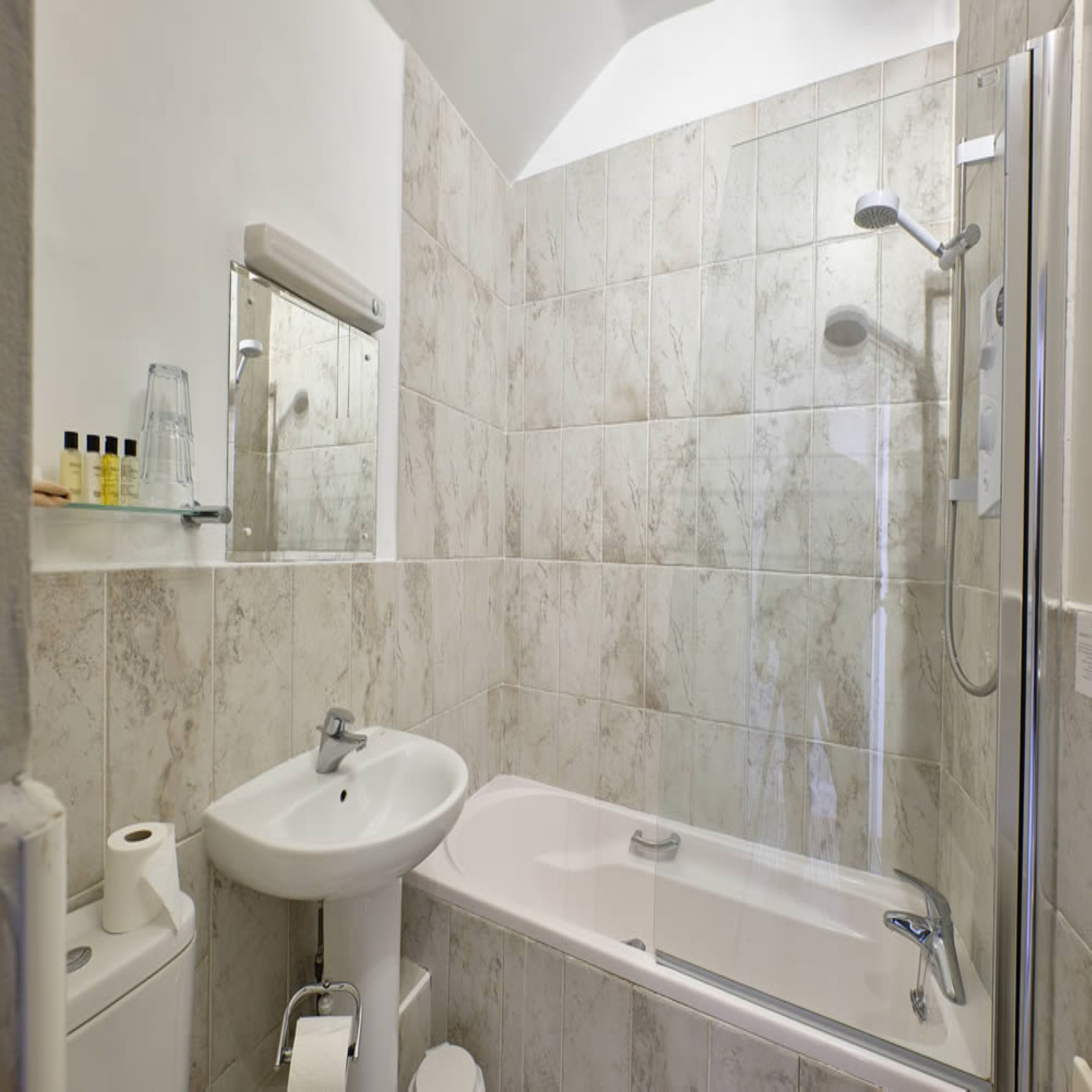 A modern bathroom with a marble-tiled shower, a white sink, and a glass-enclosed bathtub.