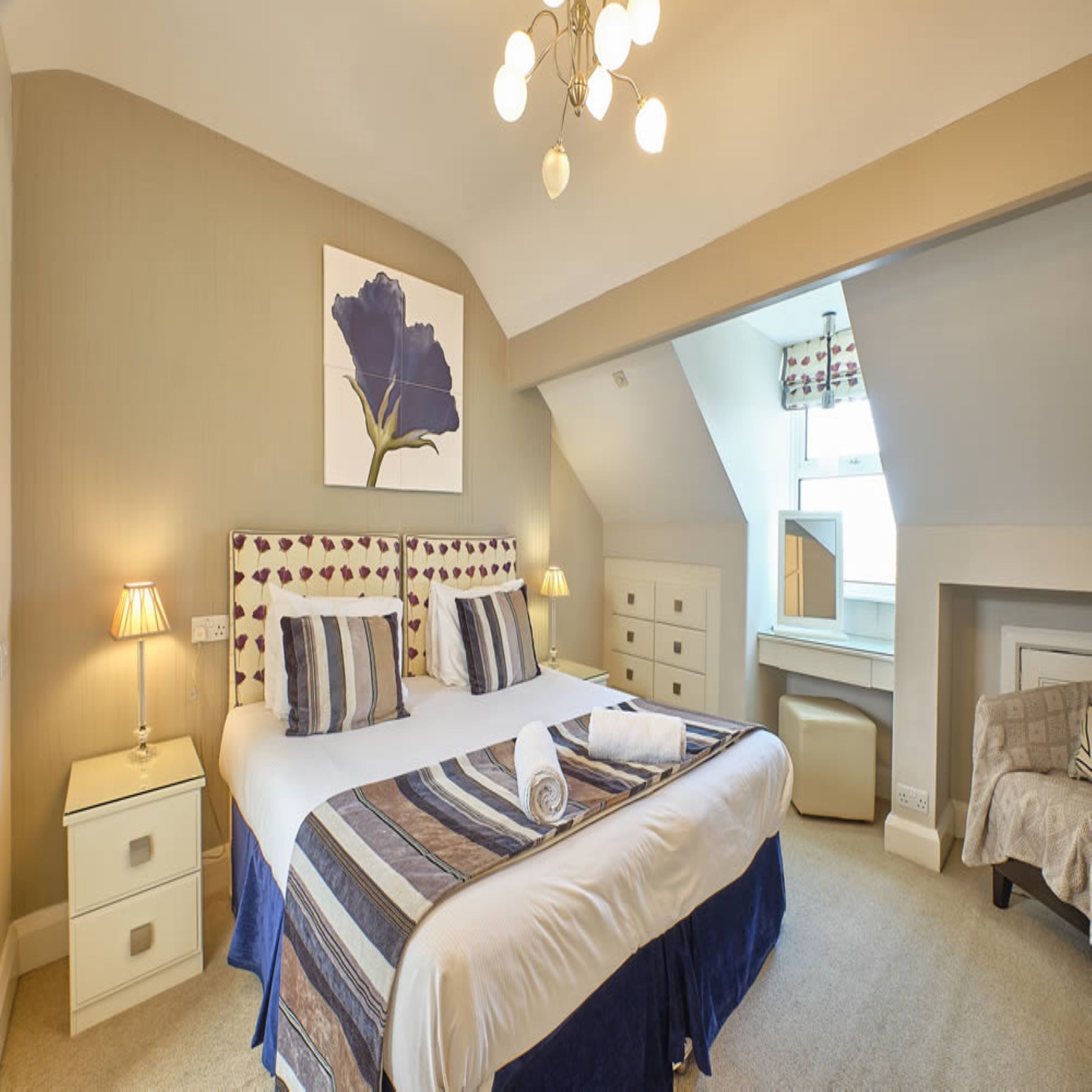 A bedroom with a large bed, bedside tables, a mirror, and a ceiling light fixture.