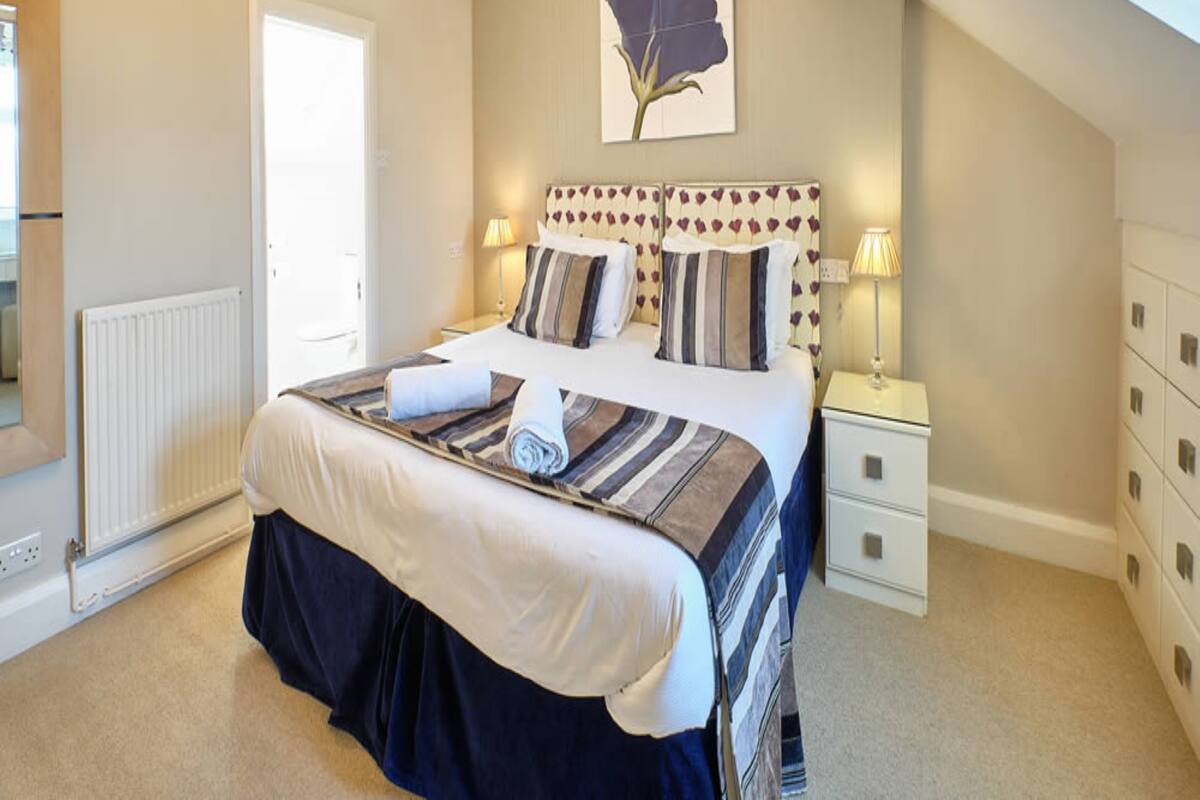 A bedroom with a bed, bedside lamps, a radiator, a window, and a ceiling light fixture.