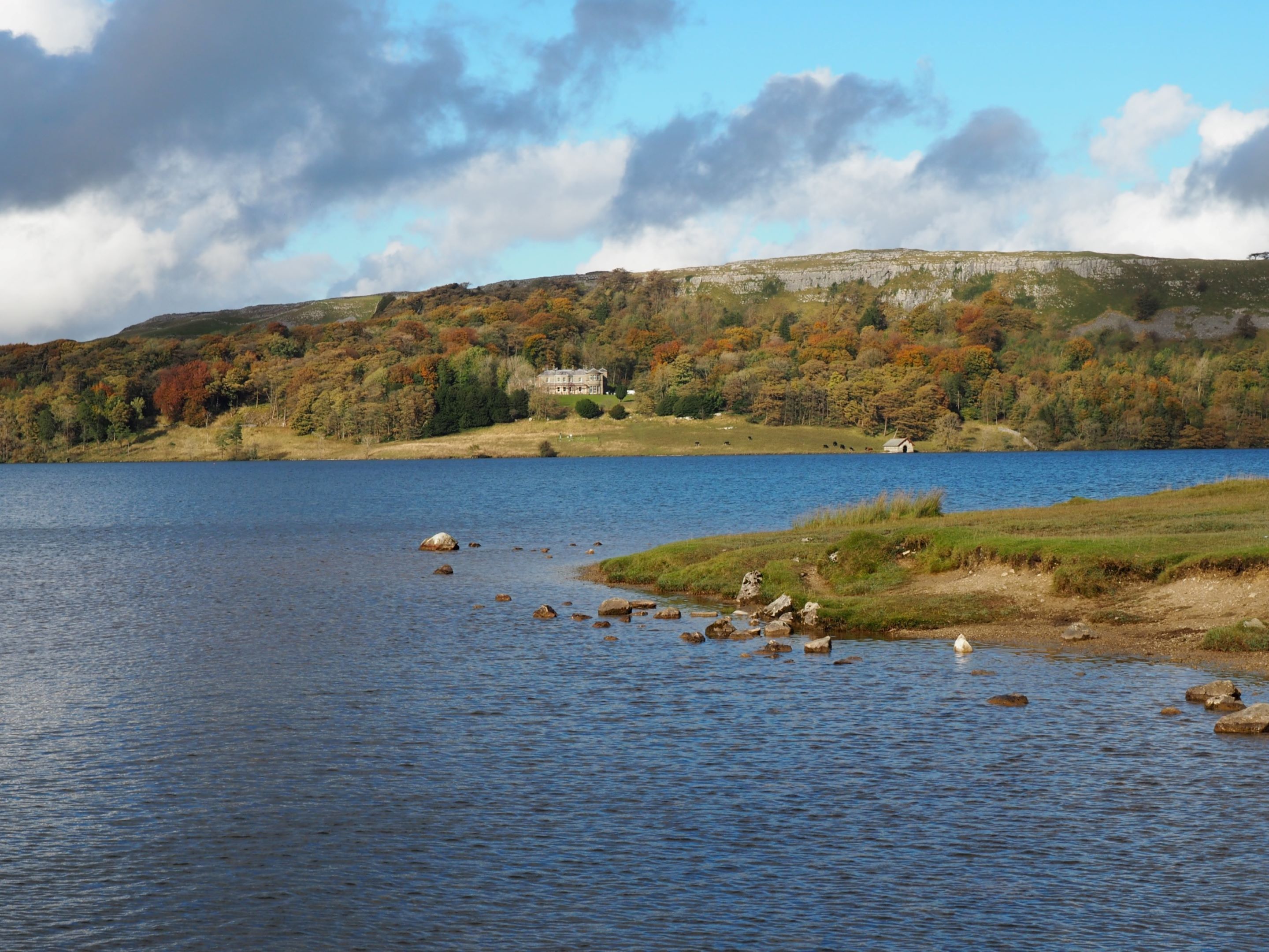 A lake with a house on a hill, surrounded by autumn-colored trees.