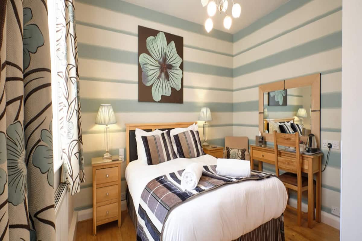 A hotel room with a bed, bedside tables, a desk, a mirror, and a large flower painting on the wall.