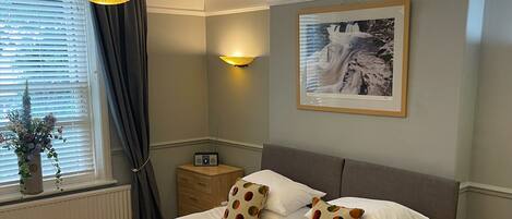 A neatly made bed with white linens and polka-dotted pillows, a bedside table with a lamp, and a framed picture on the wall.