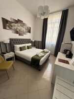 A modern hotel room with a large bed, a desk, a chair, and artwork on the wall.