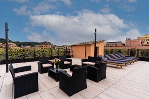 Una terraza en la azotea con mobiliario exterior, un edificio pequeño y vistas de la ciudad.