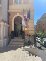 L'ingresso di un hotel con un'imponente arcata, scale che vi conducono e bandiere esposte sopra.