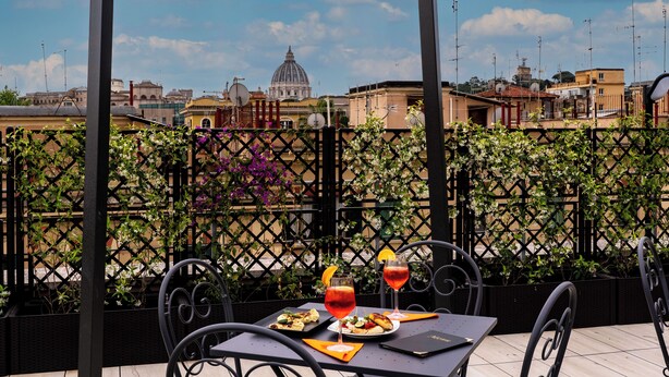 An outdoor dining area with a table set for two, featuring a meal and drinks, and a view of a domed building in the background. - Hotel Ottaviano Augusto (Rome)