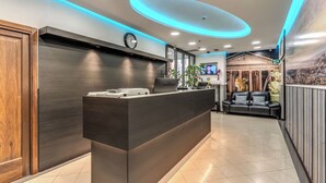 A modern reception area with a dark reception desk, a clock, and a television on the wall. - Hotel Ottaviano Augusto (Rome)