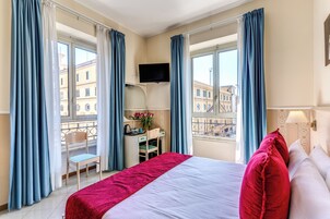 Una camera d'albergo con un letto, una scrivania, una sedia, una TV e un balcone con vista sugli edifici.