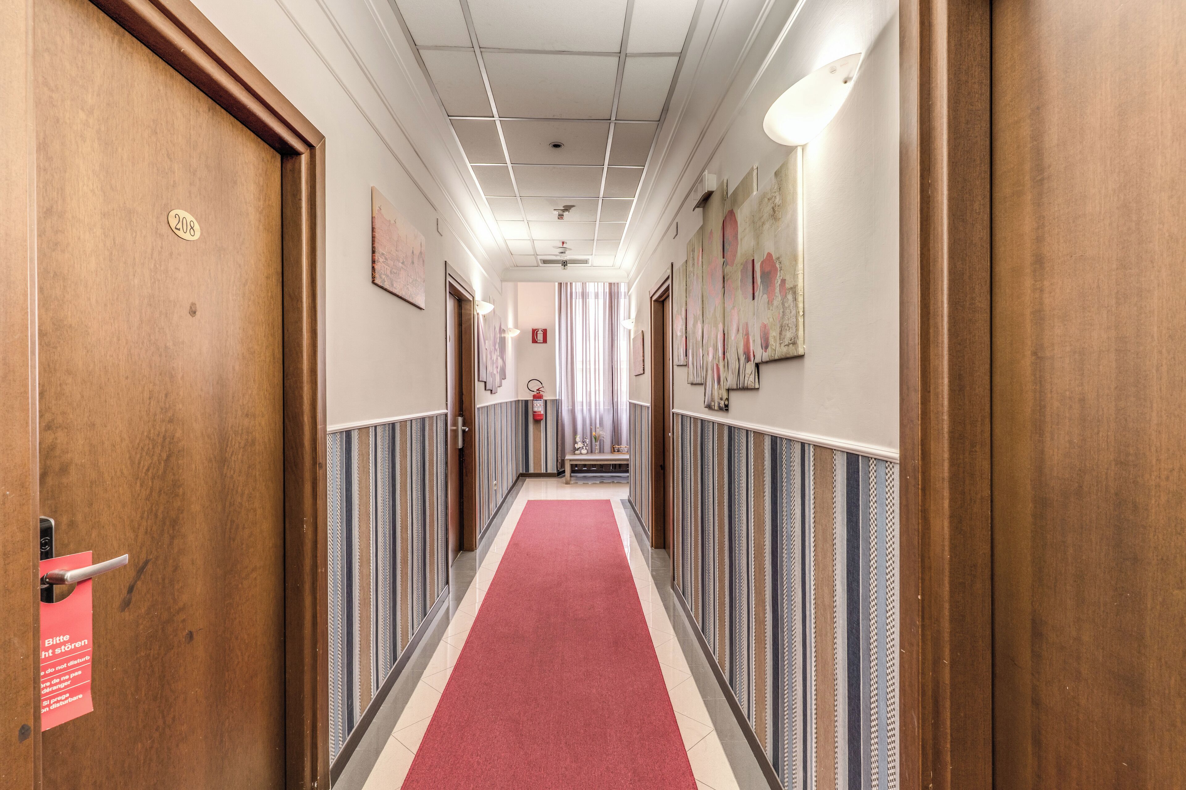 A hotel hallway with a red carpet, wooden doors, and striped walls.