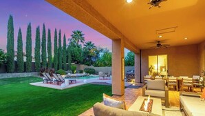 A covered outdoor patio with a fire feature, seating, and a view of the backyard. - Dreaming Tree Retreat | Pool, Spa & Fire Pit (Phoenix)