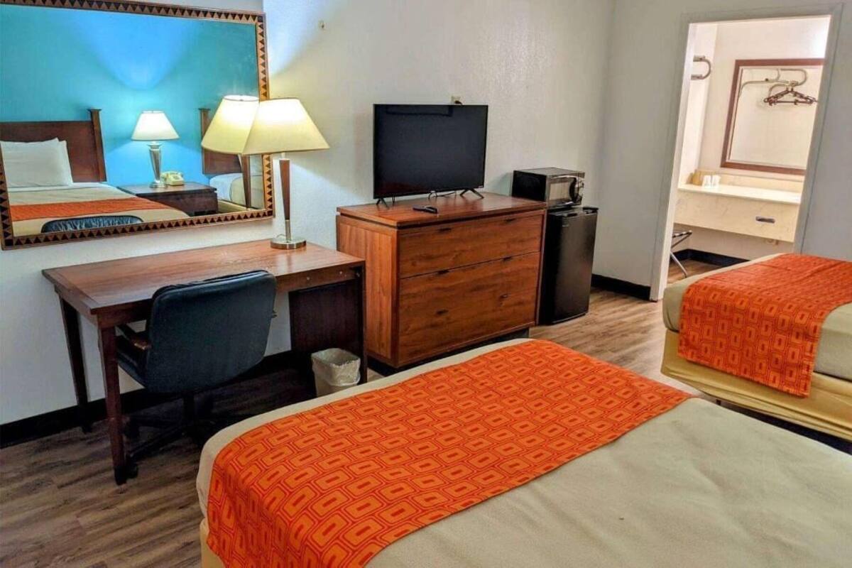 A hotel room with a bed, a desk with a chair, a television, a dresser, and a mirror.