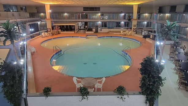 A large indoor swimming pool with multiple levels of balconies, surrounded by seating areas and potted plants. - Howard Johnson BY Wyndham Hannibal (Hannibal)