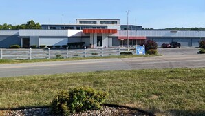 A modern building with a red awning, a parking lot, and a sign indicating an entrance. - Howard Johnson BY Wyndham Hannibal (Hannibal)