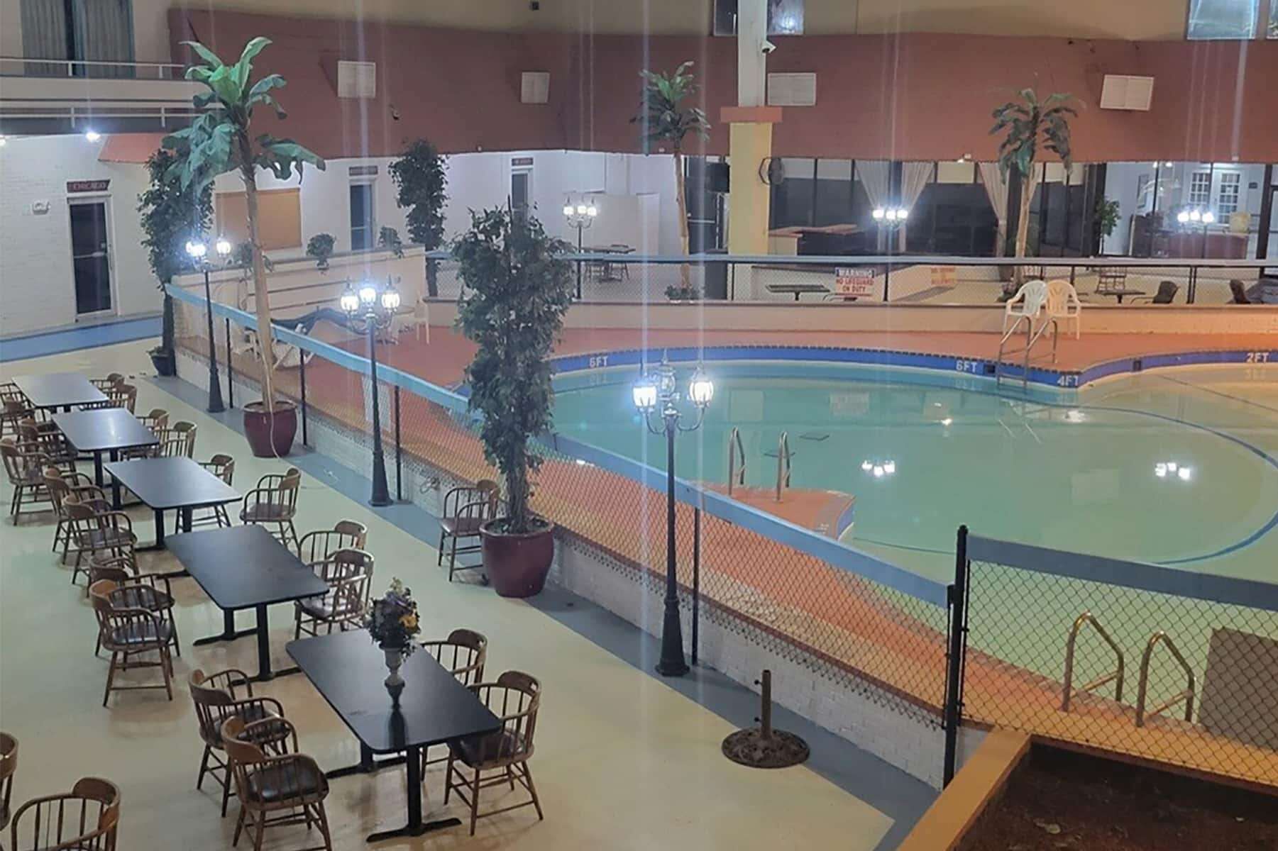 An indoor swimming pool with a surrounding dining area, tables, chairs, and potted plants.