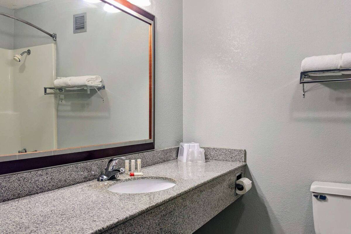 A bathroom with a granite countertop, a sink, a mirror, a towel rack, and a toilet.